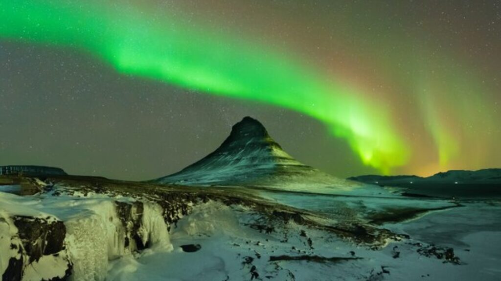 Aurora boreal verde y púrpura iluminando el cielo nocturno sobre la montaña Kirkjufell y las cascadas Kirkjufellsfoss en Islandia durante el invierno.